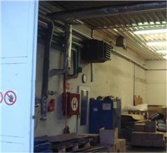 Wall-mounted industrial heater with ducting and safety signage in a warehouse.